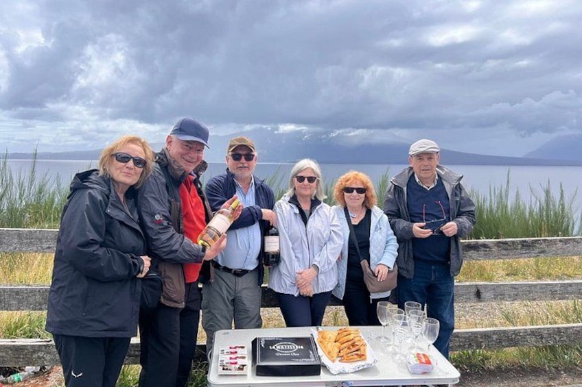 Un grupo de personas de pie junto a una mesa a orillas del lago, con comida y bebidas. 2