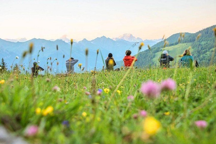 Un grupo de personas sentadas en un campo cubierto de hierba, con montañas al fondo. 2