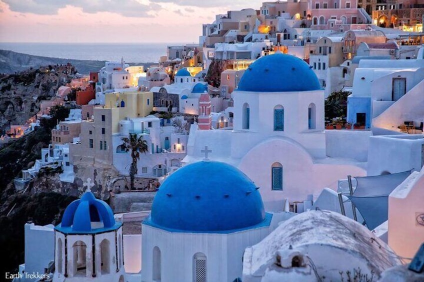 A coastal town with white and blue domed buildings, a rocky coastline, and a sunset sky. 2