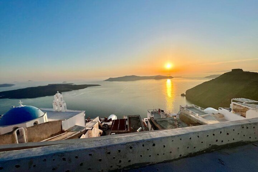 A coastal sunset view with a white building and blue dome, overlooking calm waters and distant land. 1
