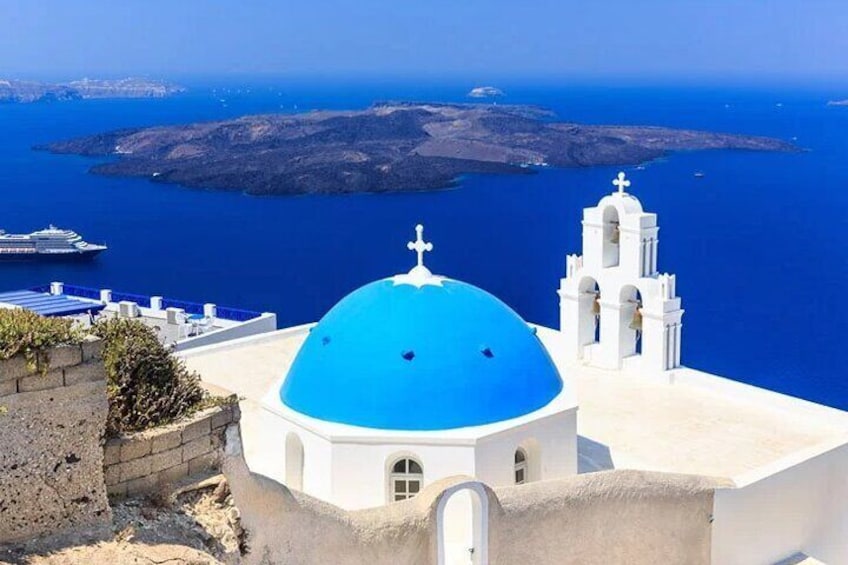 A white building with a blue dome and a bell tower, overlooking a blue sea and a distant island. 5
