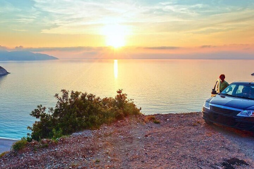 A sunset over a calm sea with a rocky shoreline and a parked car. 4