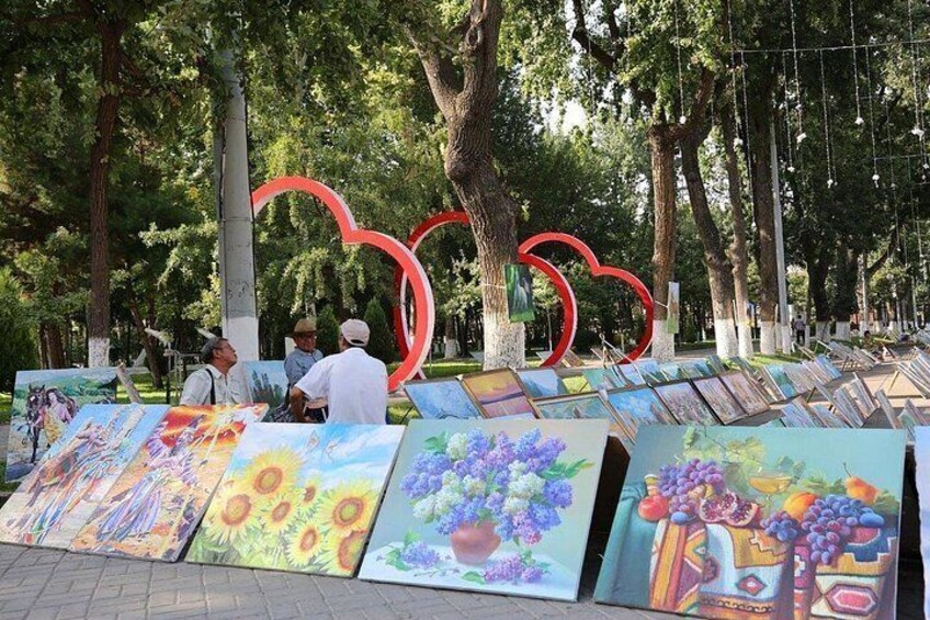 A park with trees, a heart-shaped sculpture, and paintings on the ground. 3