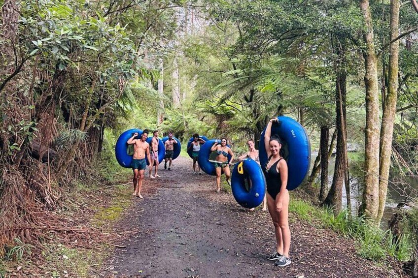 A group of people walking on a forest path, each carrying a blue inflatable tube. 4