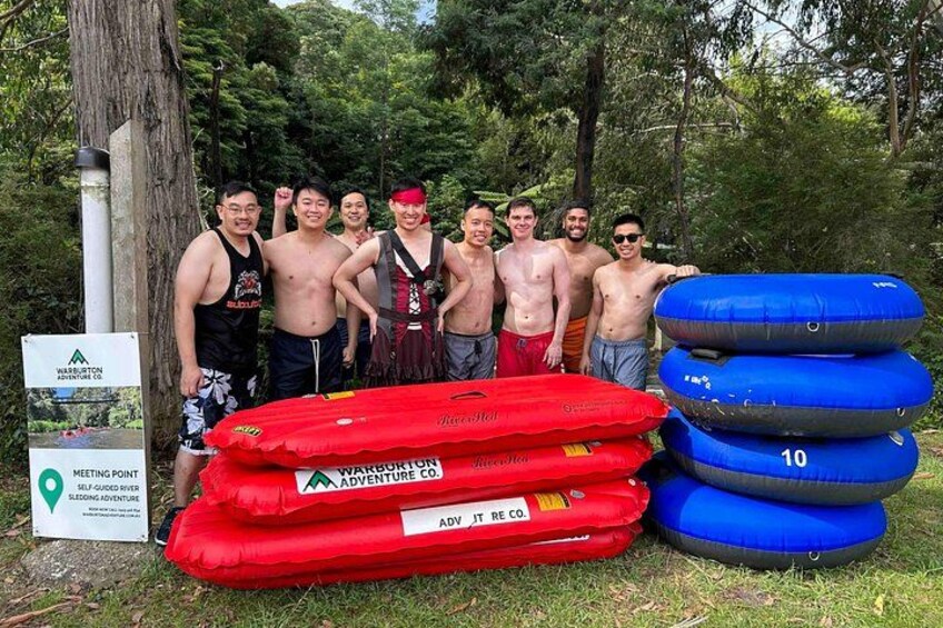 A group of people with inflatable rafts and a sign indicating a meeting point. 2