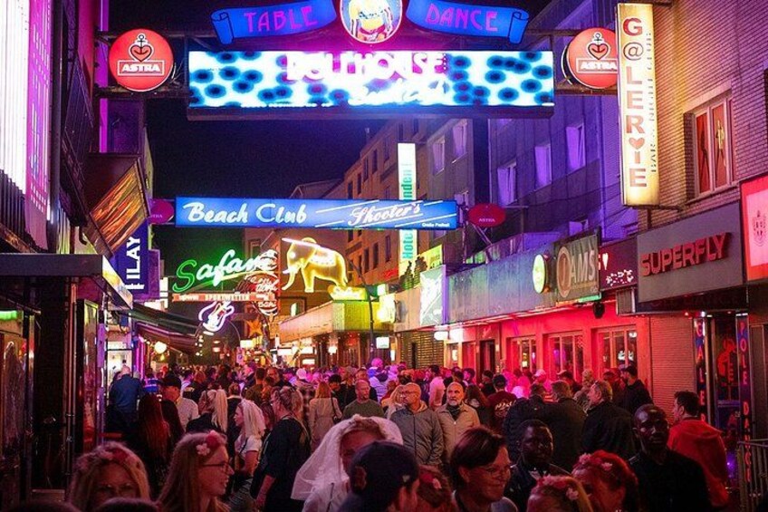 A crowded street with neon signs for a dance club, a beach club, and a safari. 4