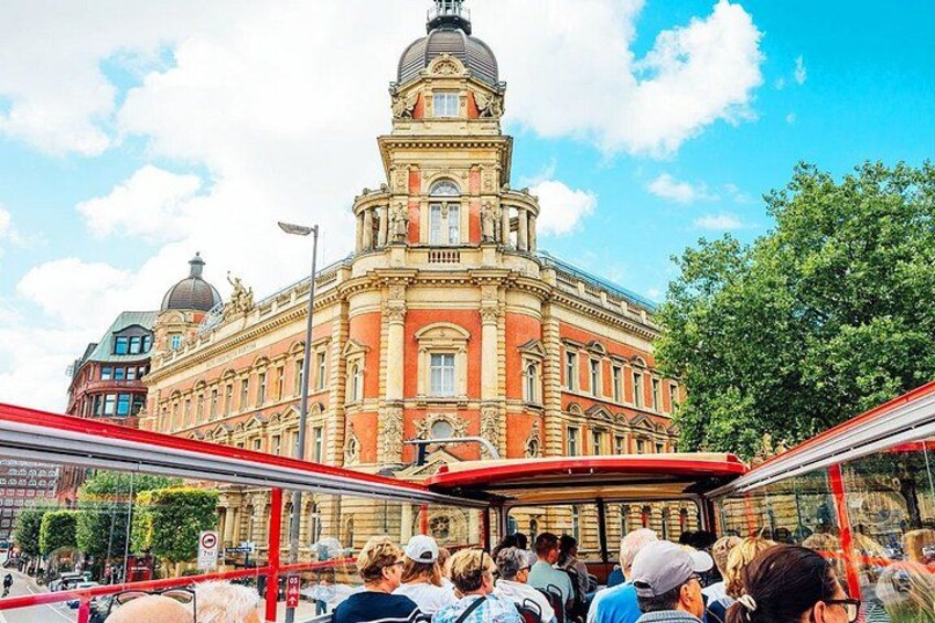 A red bus with passengers, a large ornate building with a dome, and a clear blue sky. 2