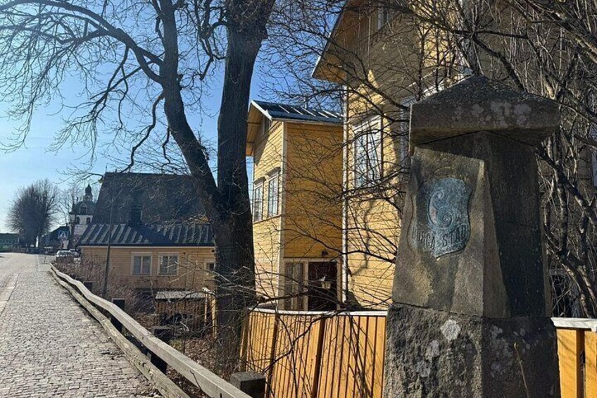 Una calle adoquinada, un edificio amarillo y un monumento de piedra con un escudo. 2