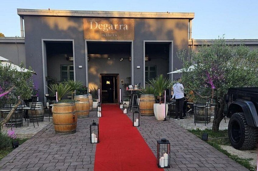 A winery entrance with a red carpet, wooden barrels, and outdoor seating. 3