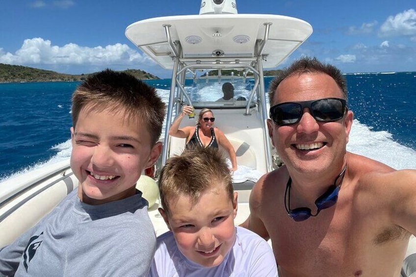 A boat with three people on board, a woman in the background, and a clear blue sea. 5