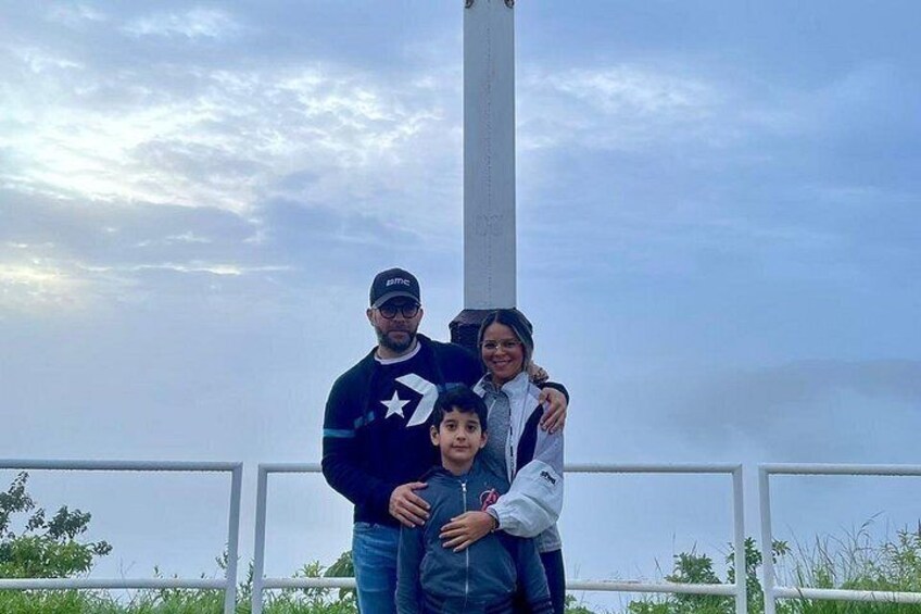 A family of three standing in front of a white column with a cloudy sky in the background. 3