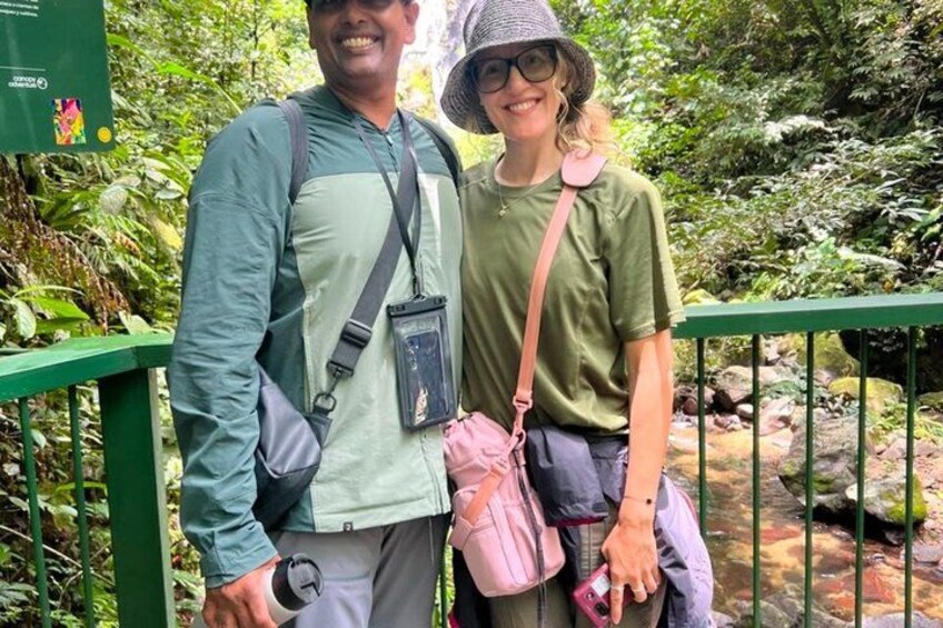 Two people standing on a bridge with greenery and a stream in the background. 3