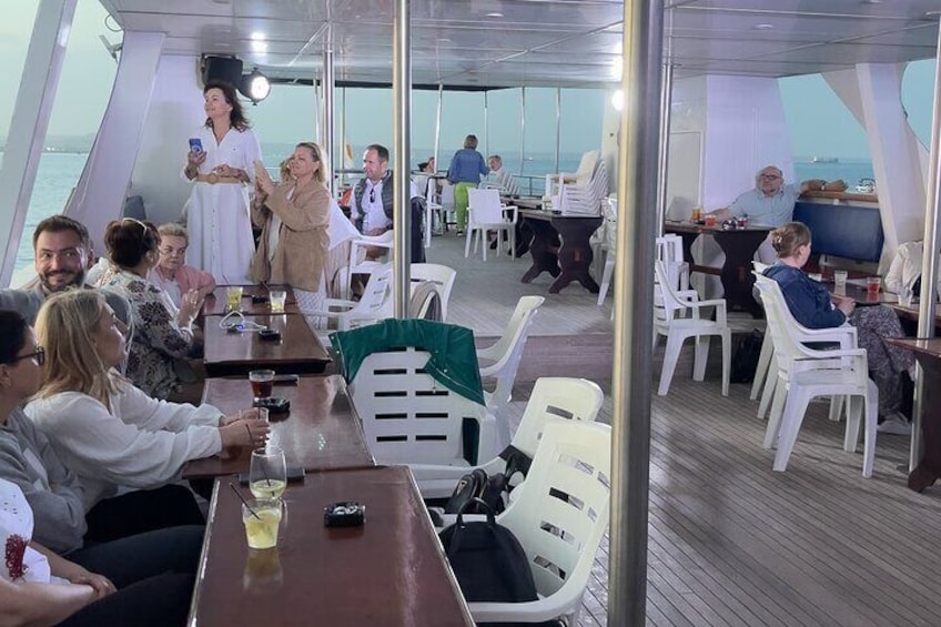 A group of people dining on a boat with tables and chairs. 4
