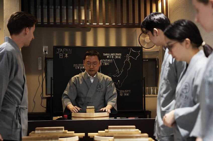 A person in a grey uniform at a wooden table with a blackboard in the background displaying a map of Japan. 4