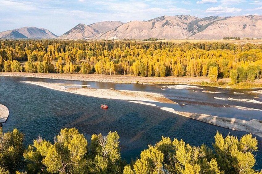 A river with a boat, surrounded by autumn-colored trees and mountains in the background. 4