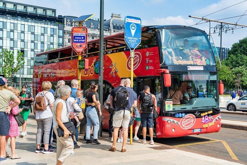 A double-decker bus at a bus stop with passengers waiting. 2