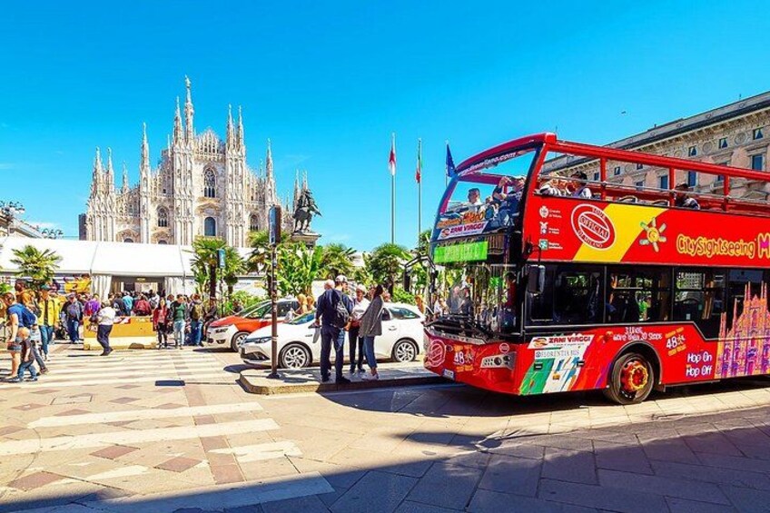 A red double-decker bus with 'CitySightseeing' branding, a cathedral with intricate architecture, and pedestrians on a sunny day. 3