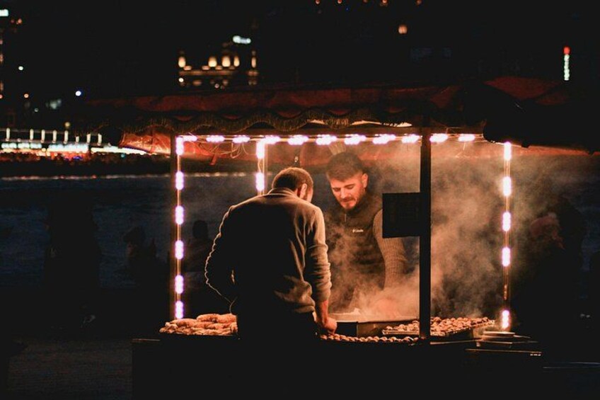A nighttime outdoor cooking setup with a grill and a person cooking. 4