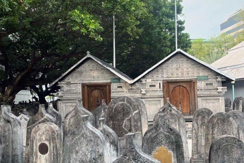 A cemetery with stone headstones and a small building with a triangular roof. 3