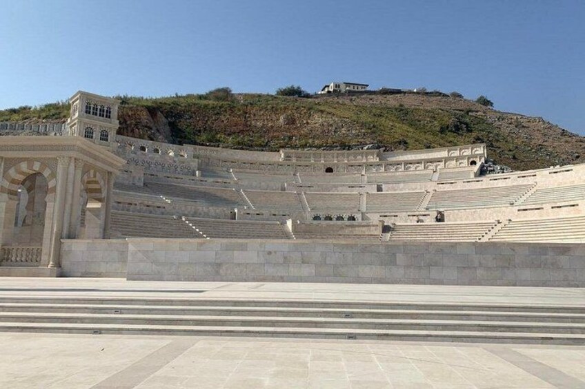 An ancient amphitheater with stone steps and a small building on a hill. 2