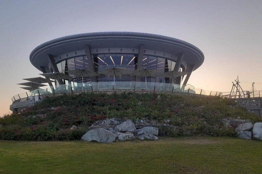 A modern circular building with a glass facade, surrounded by a landscaped area with rocks and plants. 3