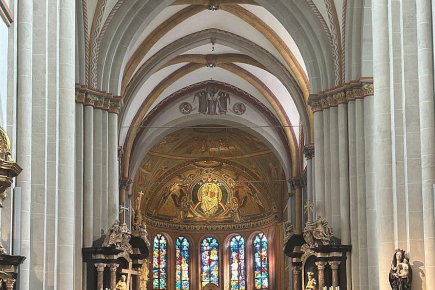 An ornate church interior with a central altar, stained glass windows, and classical columns. 3