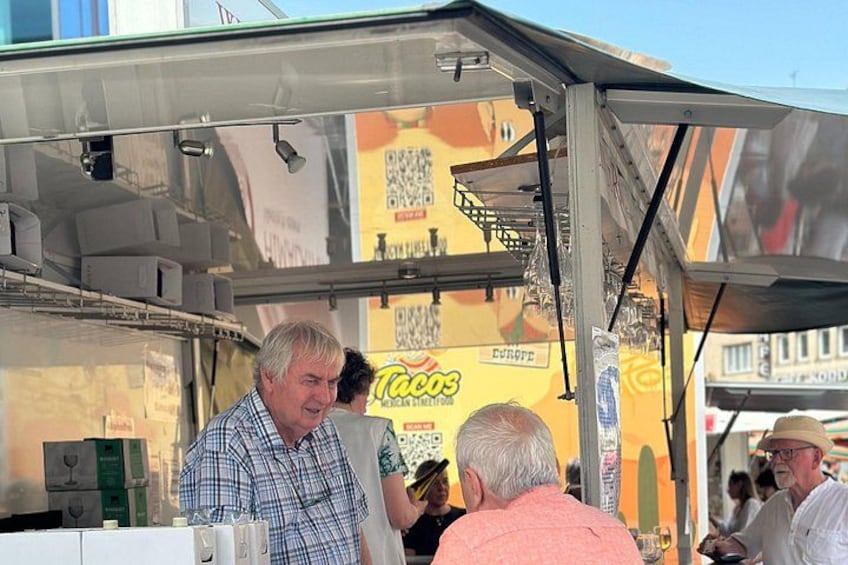 A taco stand with a yellow and orange sign, a metal roof, and a QR code. 2