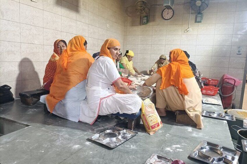 A group of people in a kitchen setting, some wearing orange headscarves, preparing food. 5