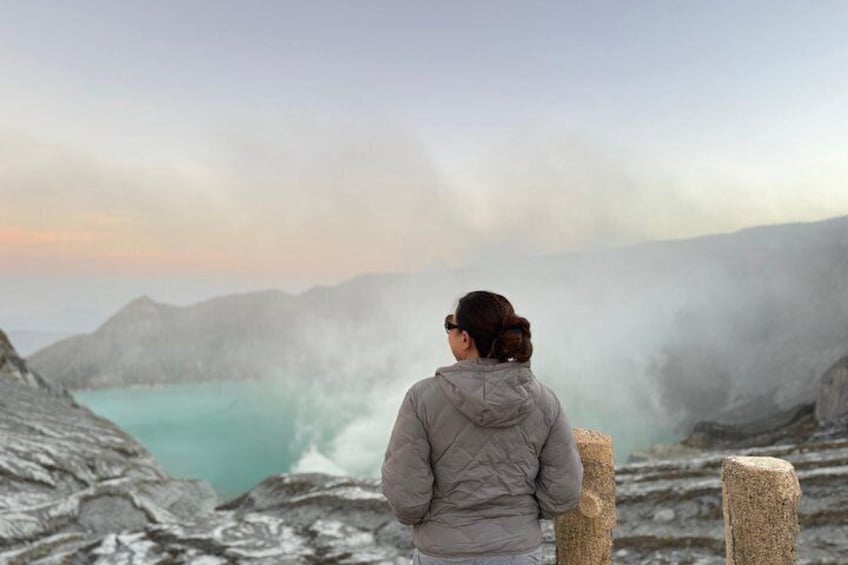 A person standing on rocky terrain overlooking a turquoise body of water with steam rising from the ground. 3