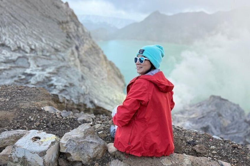 A person in a red jacket and blue beanie sitting on rocks by a glacier. 5