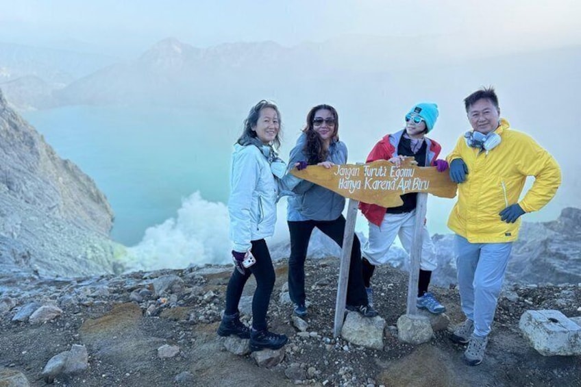 Four people standing on a rocky mountain peak with a sign in front of them. 4