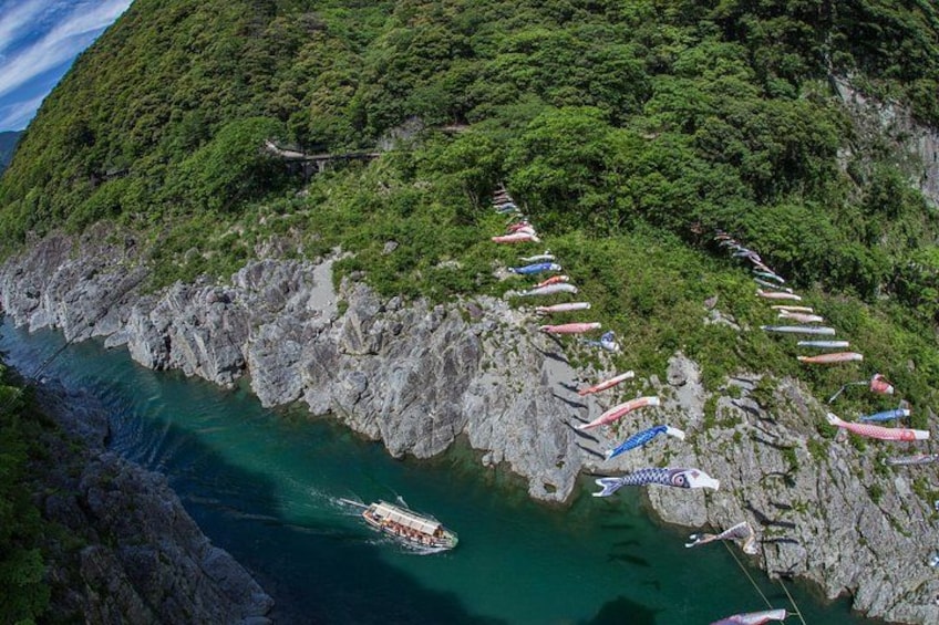 Acantilado costero con un barco anclado cerca de la orilla, un sendero estrecho con banderas coloridas y abundante vegetación. 3