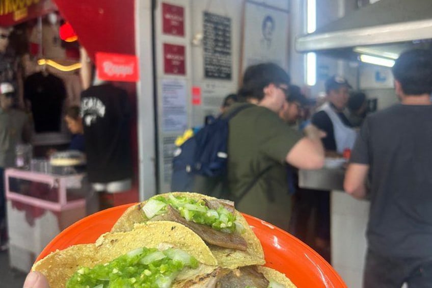 A person holding a plate with tacos in a busy food court. 2