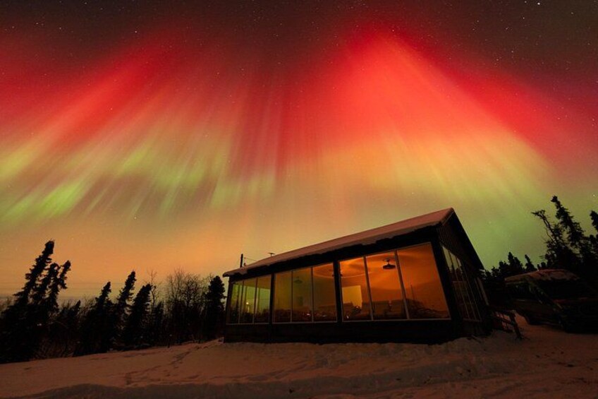 A cabin with large windows under a vibrant aurora display. 3