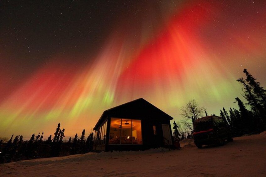 A house with a glass facade under a vibrant aurora borealis display. 1