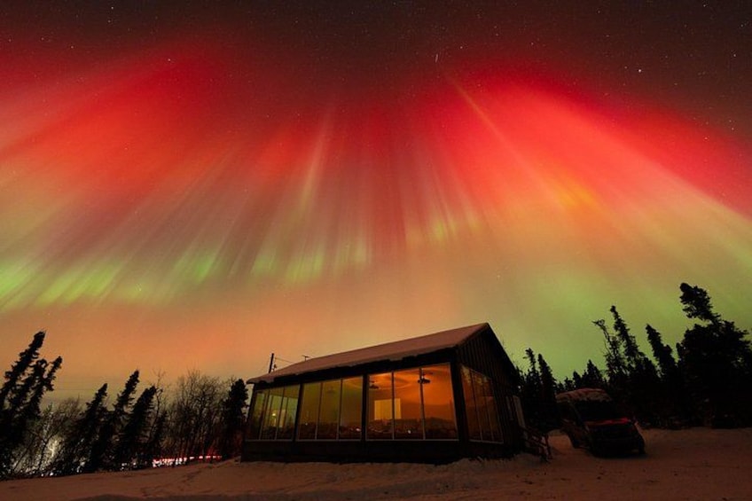 A wooden cabin with a glass facade, surrounded by snow and trees, under a vibrant aurora borealis display. 4