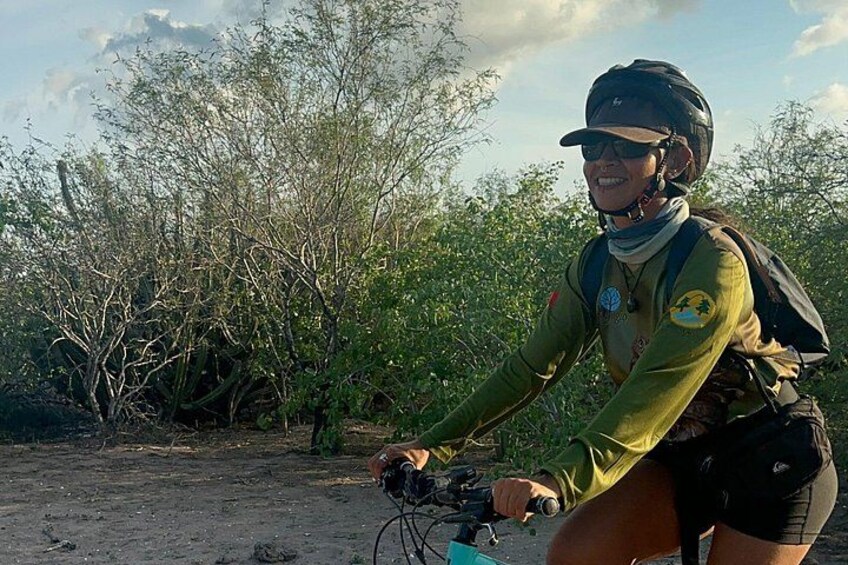 A person riding a bicycle in a natural setting with sparse vegetation and trees. 3