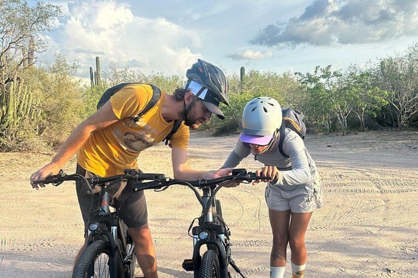 Two people on bicycles in a desert setting with sparse vegetation. 4