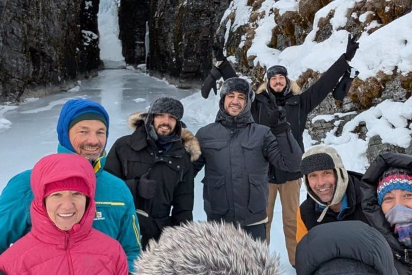 En gruppe mennesker står på en snebelagt sti med et vandfald i baggrunden. 3