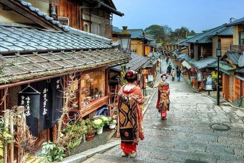 A traditional Japanese street with wooden buildings, a person in traditional attire, and potted plants. 4