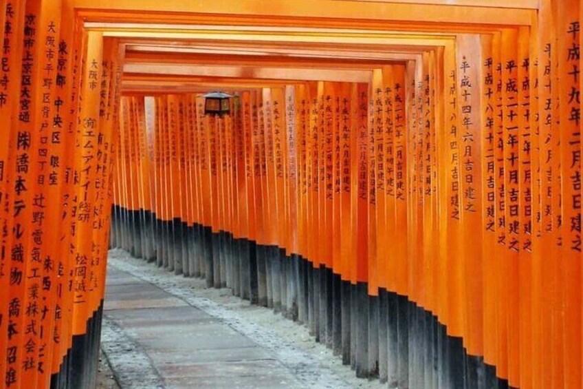 A corridor lined with orange torii gates with Japanese inscriptions. 3