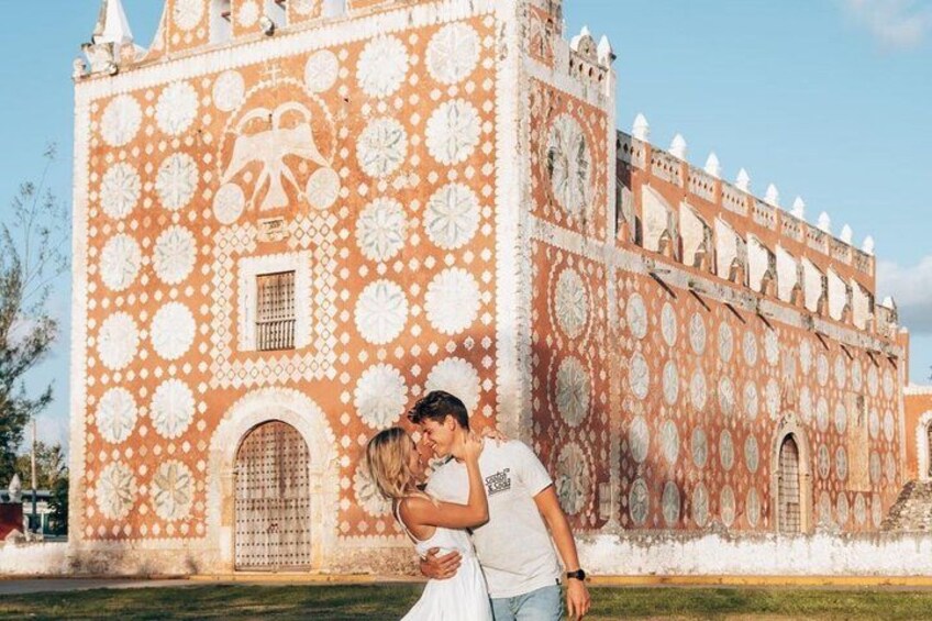 A couple embracing in front of a building with intricate white patterns and a clock tower. 2