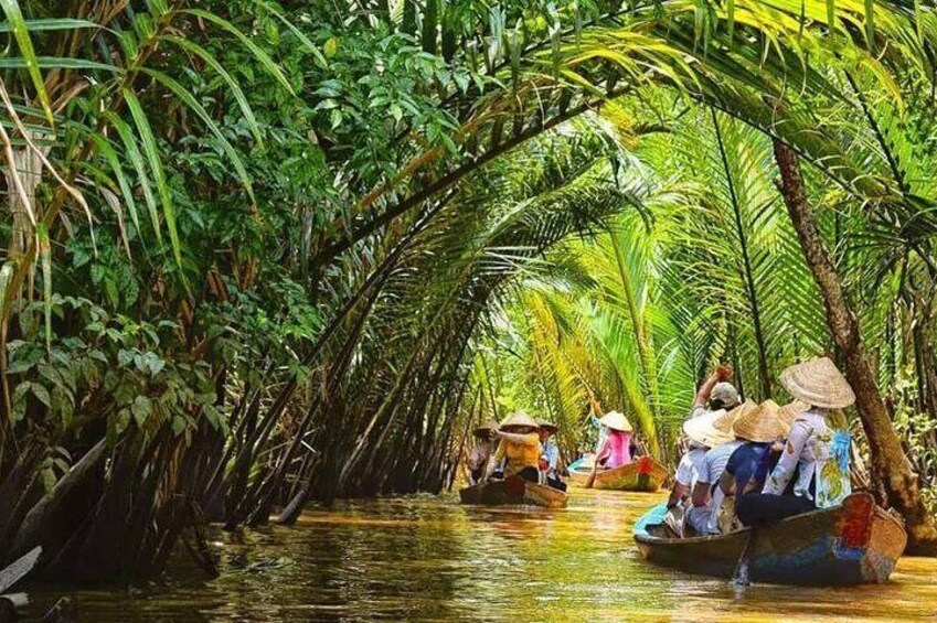 A narrow waterway flanked by dense palm trees, with people in traditional boats. 1