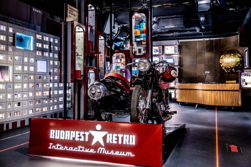 A motorcycle in a museum setting with a sign reading 'Budapest Retro Interactive Museum.' 5