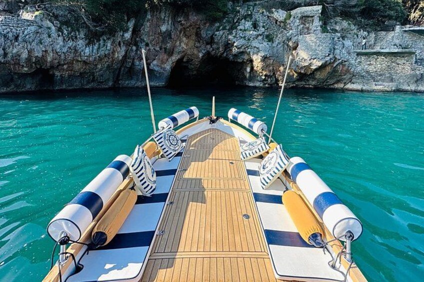 A boat with a wooden deck and blue-striped cushions, anchored near rocky cliffs in clear blue water. 5
