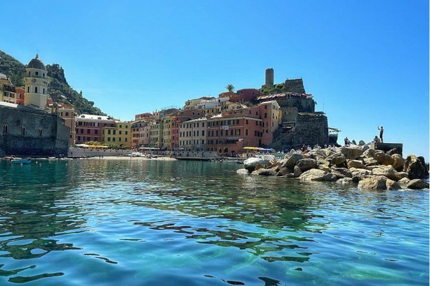 A coastal town with colorful buildings, clear blue water, and rocky shoreline. 1