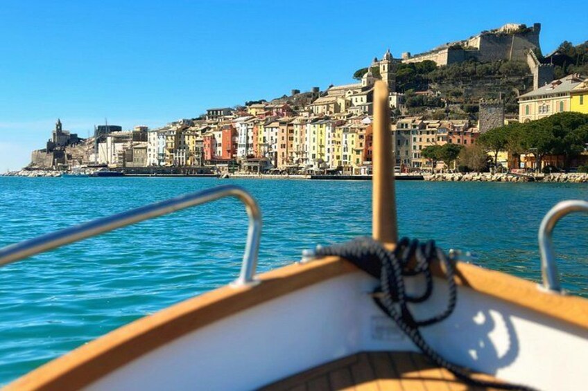 A boat's bow with a rope and metal railings, water, and a colorful coastal town with buildings and a fort on a hill. 2