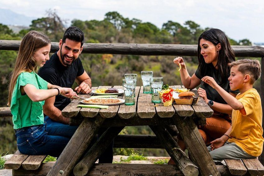 A family dining at an outdoor wooden table with food and drinks. 1