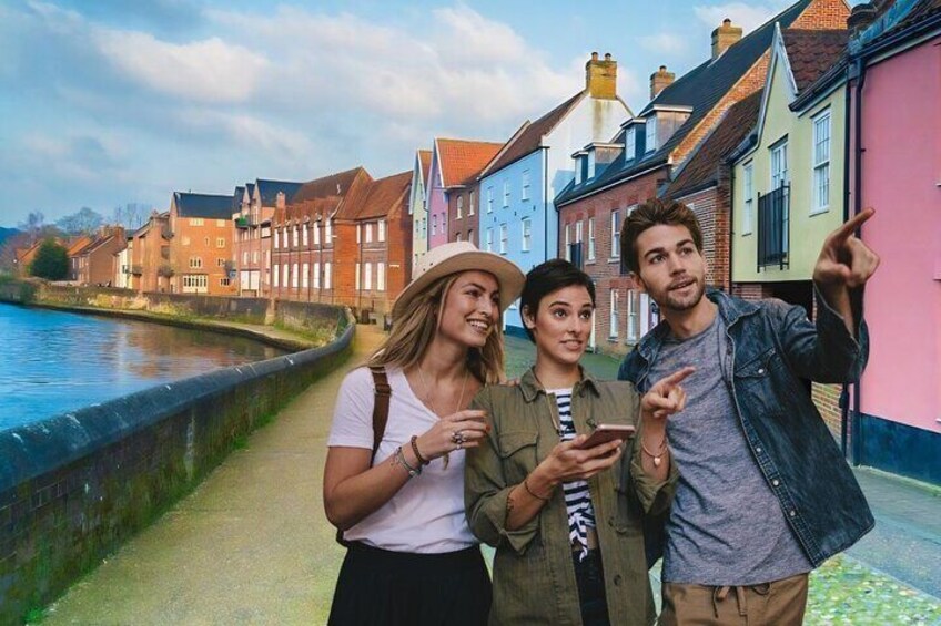 Three people standing on a riverside path with colorful buildings in the background. 1