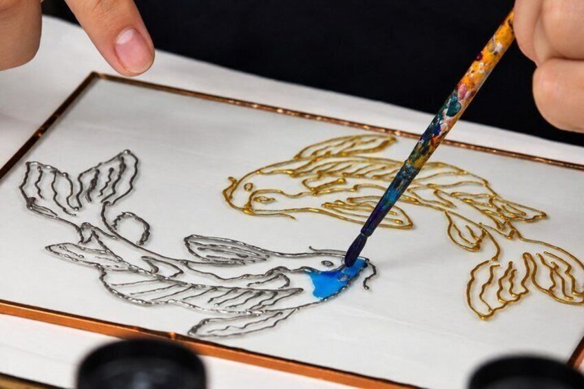 A person painting a floral design on a framed canvas. 5